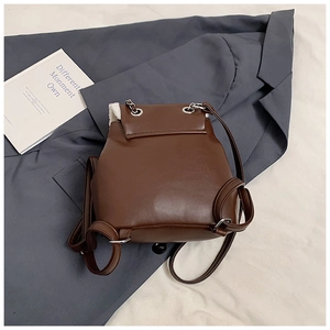 Detail of a brown leather mini backpack featuring white faux shearling trim and silver chains