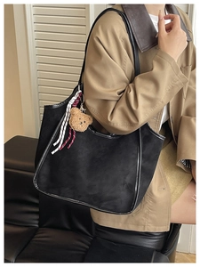 Close-up of black suede bucket bag with cute bear charm and striped woven strap decoration