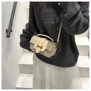 Detail of cream leather handbag with gold H buckle on model in minimalist stairs setting