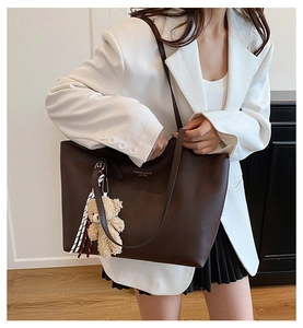 Détail d'un sac cabas en similicuir marron foncé avec un ours en peluche et un ruban chic