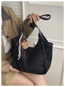 Detail of black suede tote bag featuring a plush bear pendant and woven red-white cord
