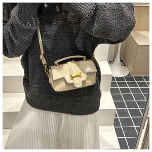 Detail of a creamy white leather shoulder bag with gold H-buckle worn on knit sweater