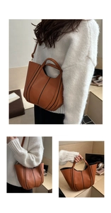 Detail of brown leather bucket bag featuring black vertical stitching and dual straps