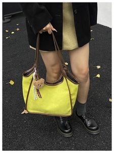 Detail of yellow-green canvas bucket bag with brown leather trim and bear charm