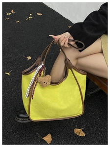 Close-up of yellow suede bucket bag with leather handles and a brown plush bear charm