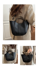 Detail of black bucket bag with vertical stitching, dual handles and adjustable strap