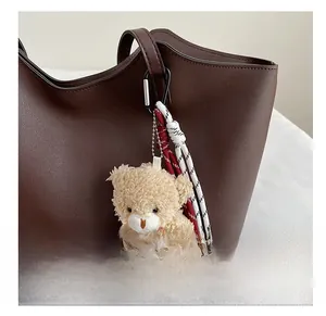 Gros plan d'un ours en peluche beige avec cordes tressées sur un sac en cuir marron