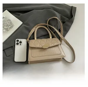 Détail d'un sac à bandoulière matelassé beige avec texture croco sur un costume