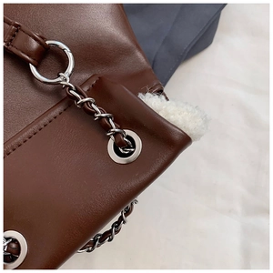 Macro detail of dark brown leather bag with silver chain, eyelets and faux fur lining