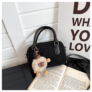 Détail d'un sac à main en daim noir avec un charmant mouton en peluche beige et deux poignées