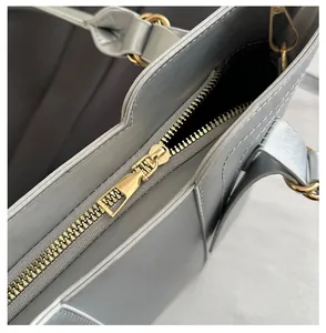 Close-up of premium light gray textured leather tote with polished gold zipper detail