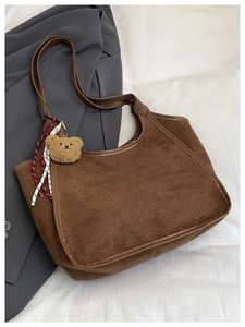 Close-up of brown suede bucket bag with leather handles and cute plush bear charm detail