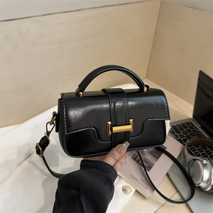 Chic black glossy square handbag with gold buckle and top handle in a lifestyle setting
