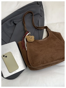 Detail of brown suede bucket bag with leather trim and cute bear charm on white fabric