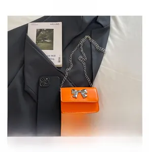 Mini orange crossbody bag with silver bow shown next to a smartphone for size comparison