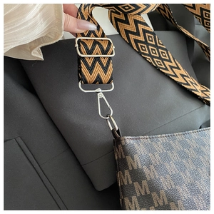 Detail of a chic shoulder bag with M-pattern print and a wide geometric woven strap