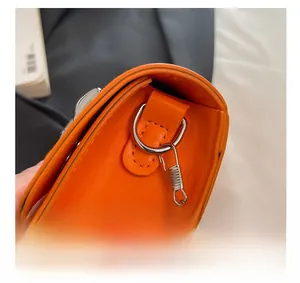 Macro shot of silver metal chain spring clasp and D-ring on bright orange handbag