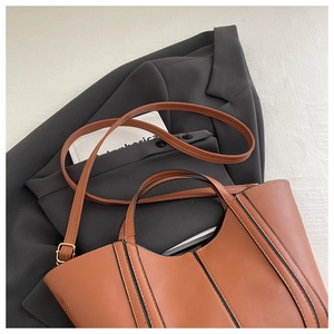 Detail of a brown faux leather tote bag with black contrast stitching and golden hardware