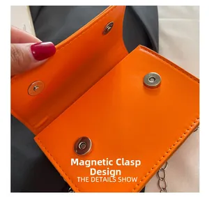 Close-up of orange leather bag featuring dual magnetic buckles and silver chain strap