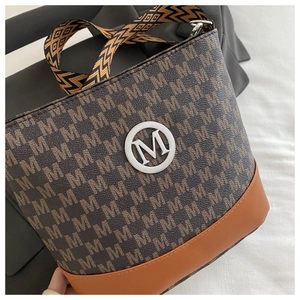Detail of a contrast color bucket bag featuring M-pattern canvas and wide woven strap