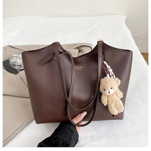 Détail d'un sac cabas en cuir marron avec texte doré et pendentif ours en peluche