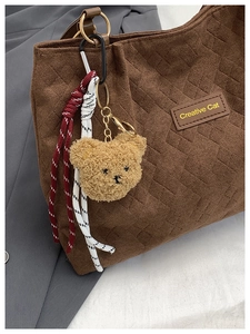 Macro shot of coffee brown quilted tote bag with gold ring and plush bear charm