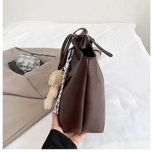 Détail du sac cabas marron foncé avec breloque ours et ruban sur le profil latéral