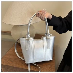 Detail of silver metallic handbag with vertical stitching and gold hardware on a wooden surface