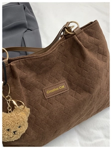 Close-up of quilted tote bag featuring a leather brand tag and plush bear charm