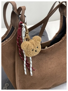 Plush brown bear charm with braided rope and metal buckle on a suede bucket bag