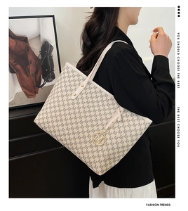 Detail of cream monogram tote bag with gold M pendant and all-over pattern on a model
