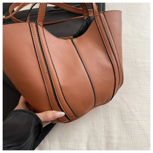 Close-up of brown faux leather tote bag with black trim and adjustable shoulder strap