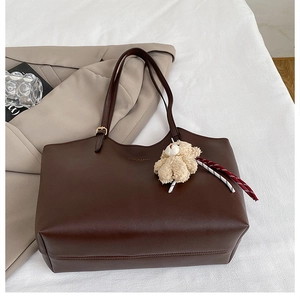 Détail de sac cabas en similicuir marron foncé avec breloque ours et sangle réglable
