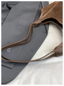 Detail of dark brown hobo bucket bag in suede and leather over a grey blazer jacket