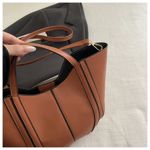 Brown structured tote bag detail with black trim edges and gold metal strap hooks