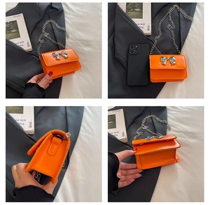 Close-up of a mini orange crossbody bag featuring a silver metal bow and chain strap