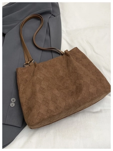 Detail of a brown quilted suede tote bag with leather handles on a white fabric surface