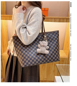 Detail of checkered tote bag with plush bear charm worn by a model in casual style