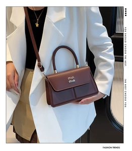 Detail of a chocolate brown leather handbag featuring a gold 3D logo and elegant top handle