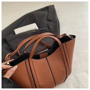 Detail of a brown leather handbag with black trim and gold hardware on grey clothing