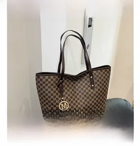 Close-up of brown tote bag with M-letter print and golden circular metal charm