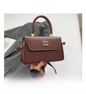 Detail of a brown leather bag showing gold hardware handles and brand logo plaque