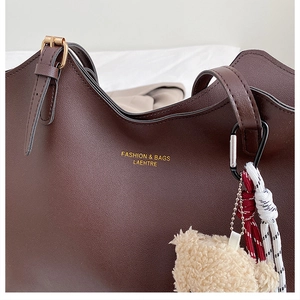 Gros plan d'un sac cabas marron foncé avec détails dorés et breloque ours en peluche