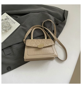 Détail du sac beige en similicuir avec texture crocodile et fermoir doré sur un magazine