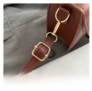 Detail of dark brown leather handbag showing adjustable strap with gold metal buckle