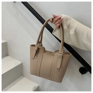 Close-up of stylish beige bucket bag with metal rings and elegant handle details