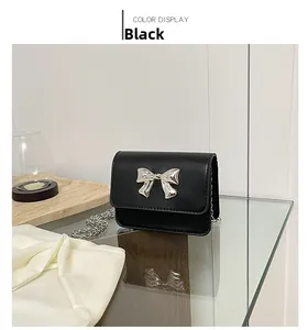Detail view of black mini crossbody bag featuring a silver bow clasp and chain strap