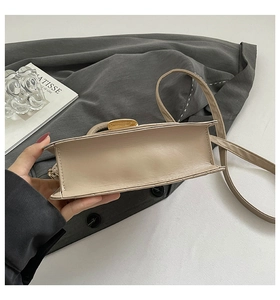 Détail d'un sac bandoulière beige montrant les coutures et la boucle en métal doré