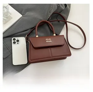 Detailed view of brown leather handbag with a gold logo and adjustable shoulder strap