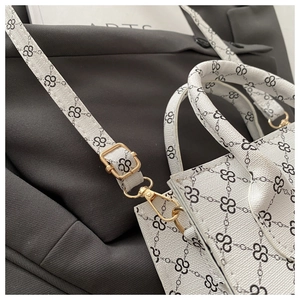 Detailed close-up of golden metal buckle and black logo pattern on white handbag